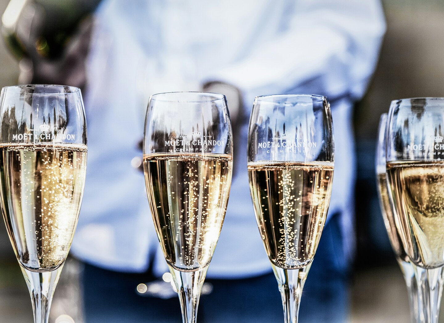 Vier Champagnergläser mit Moët & Chandon-Logo stehen nebeneinander, gefüllt mit sprudelndem Champagner.
